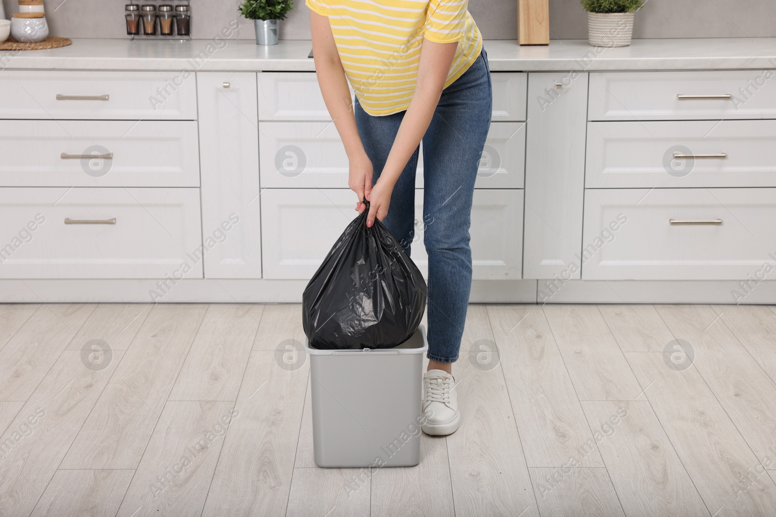 Photo of Woman taking garbage bag out of trash bin in kitchen, closeup