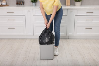 Photo of Woman taking garbage bag out of trash bin in kitchen, closeup