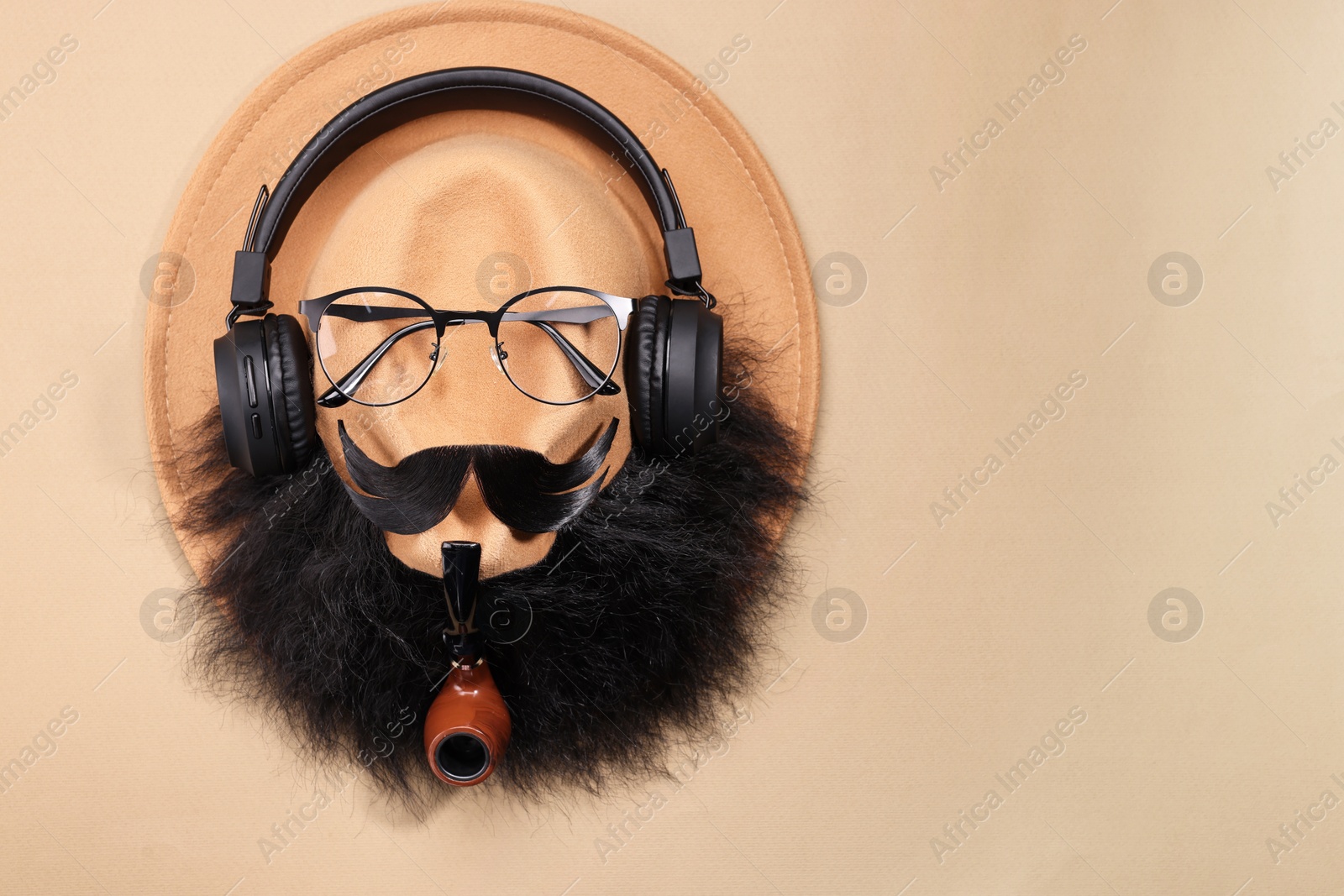 Photo of Man's face made of artificial mustache, beard, glasses and hat on beige background, top view. Space for text