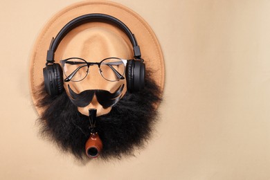 Photo of Man's face made of artificial mustache, beard, glasses and hat on beige background, top view. Space for text