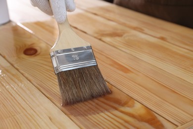 Photo of Man varnishing wooden surface with brush, closeup