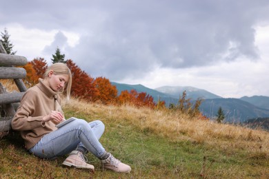 Photo of Young woman drawing on tablet in mountains, space for text