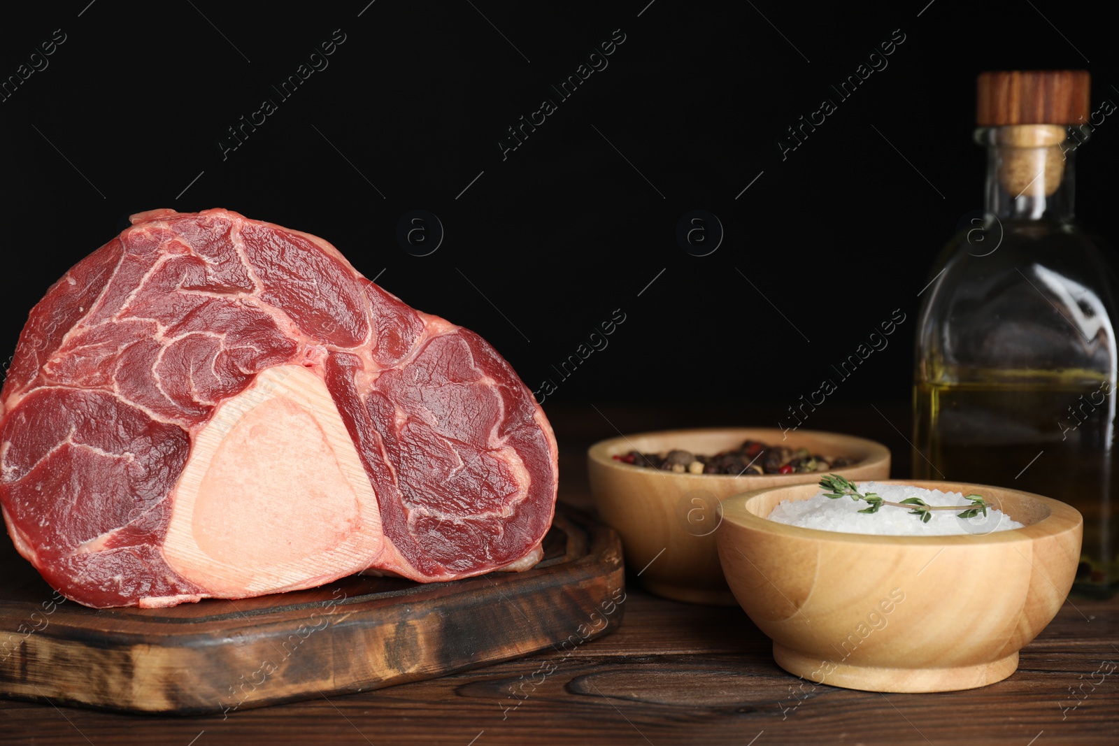 Photo of Piece of raw beef meat and spices on wooden table against black background, closeup
