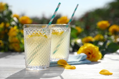 Photo of Glasses of refreshing lemonade on white wooden table in rose garden. Space for text