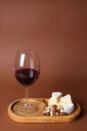 Photo of Glass of red wine, cheese and nuts on brown background, space for text