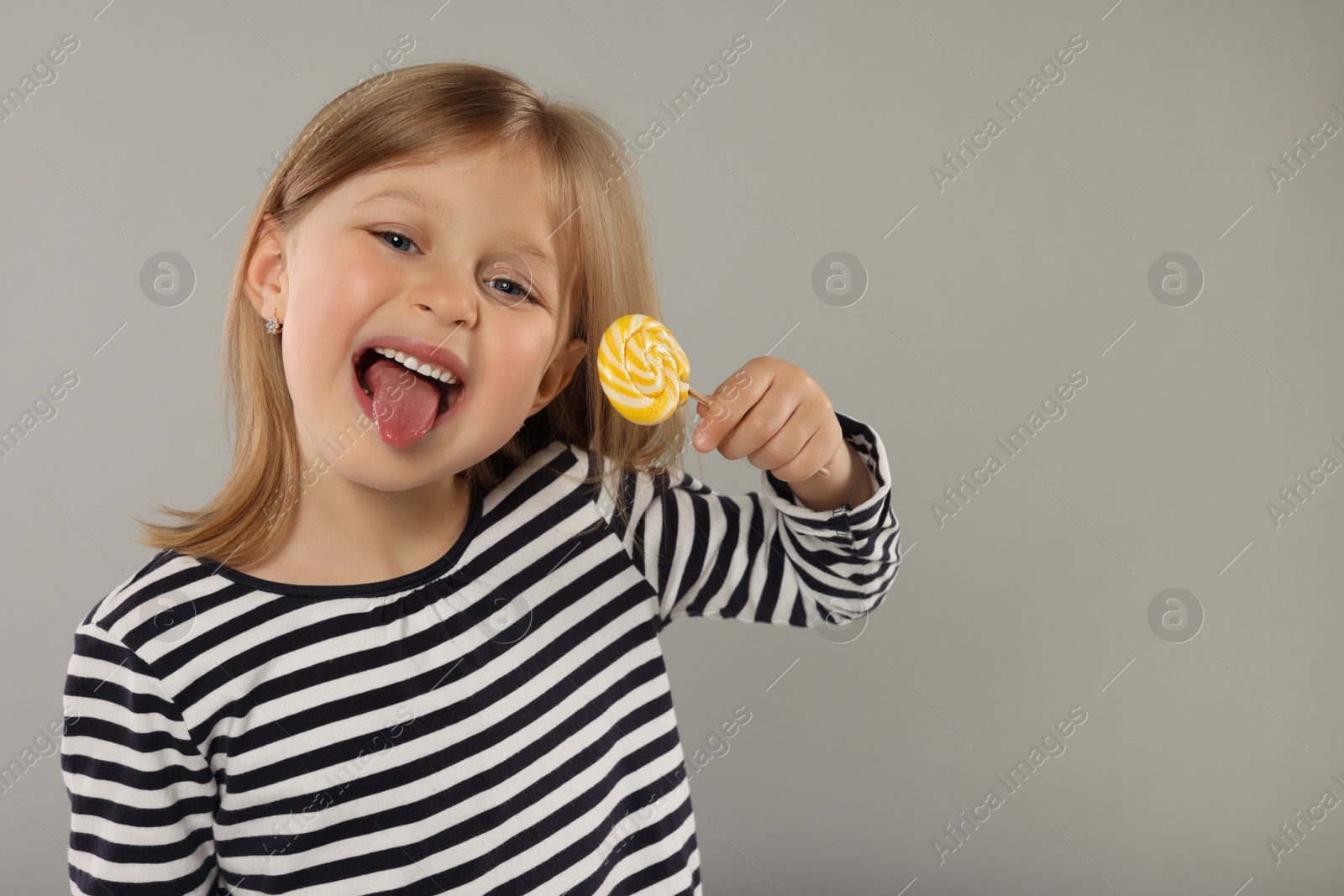 Photo of Portrait of happy girl with lollipop on light grey background, space for text