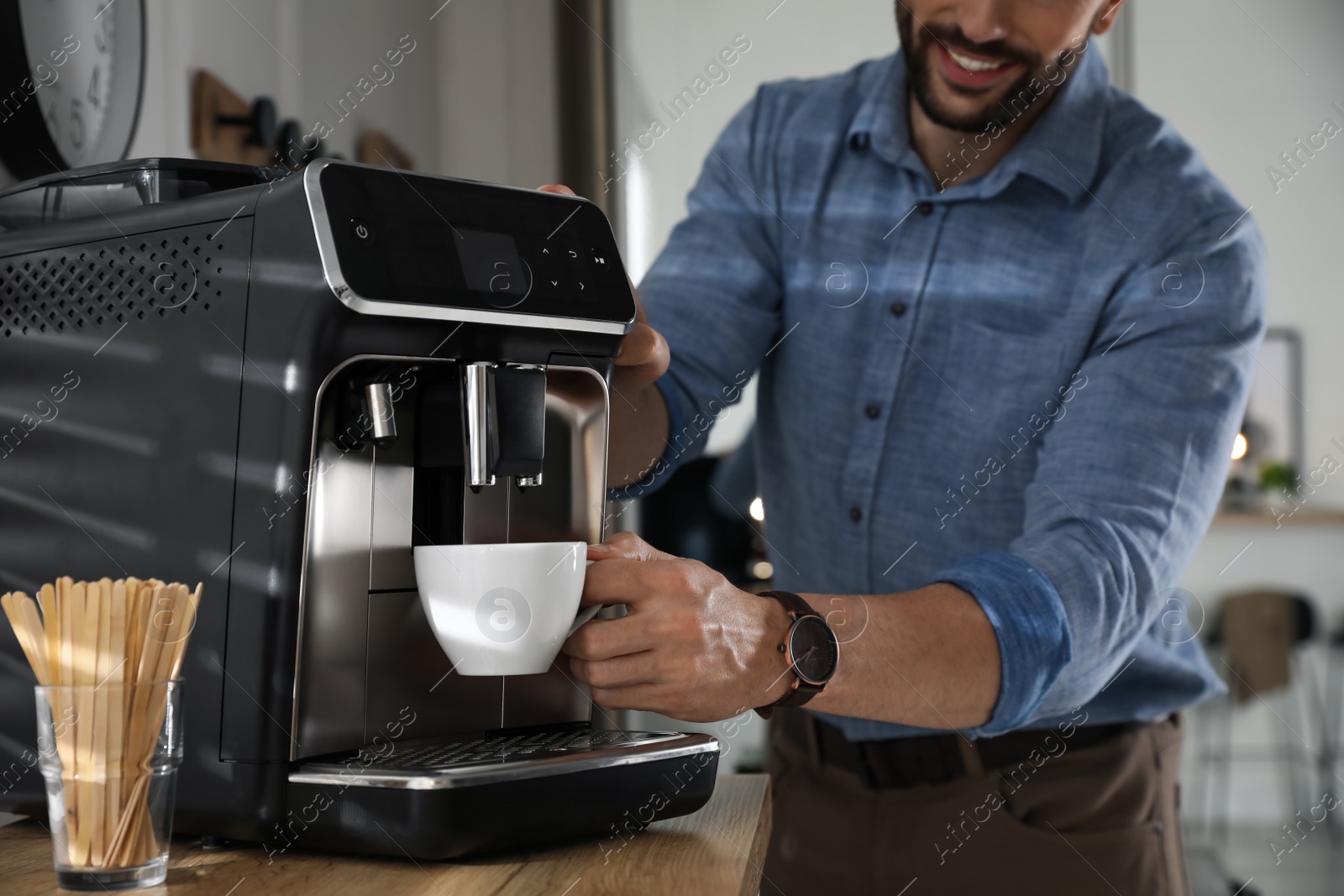 Photo of Man preparing fresh aromatic coffee with modern machine in office, closeup