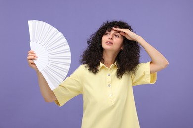Woman with hand fan suffering from heat on purple background