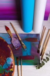 Photo of Canvas with colorful abstract painting, different brushes and wooden artist's palette on white table, above view