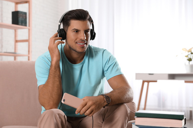 Photo of Man with mobile phone listening to audiobook on sofa indoors