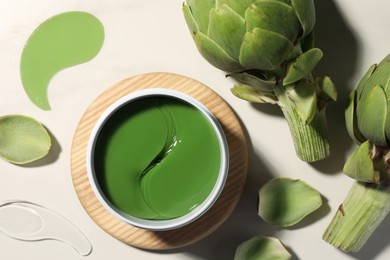 Photo of Package of under eye patches and artichokes on white table, flat lay. Cosmetic product