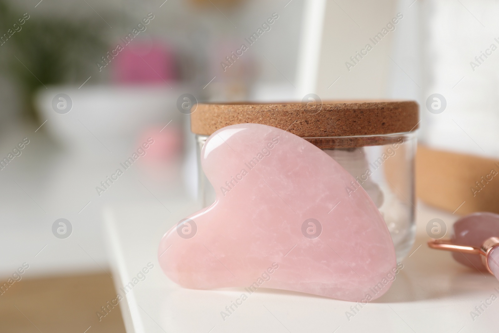 Photo of Rose quartz gua sha tool, natural face roller and toiletries on white shelf, closeup