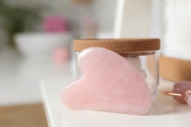 Photo of Rose quartz gua sha tool, natural face roller and toiletries on white shelf, closeup