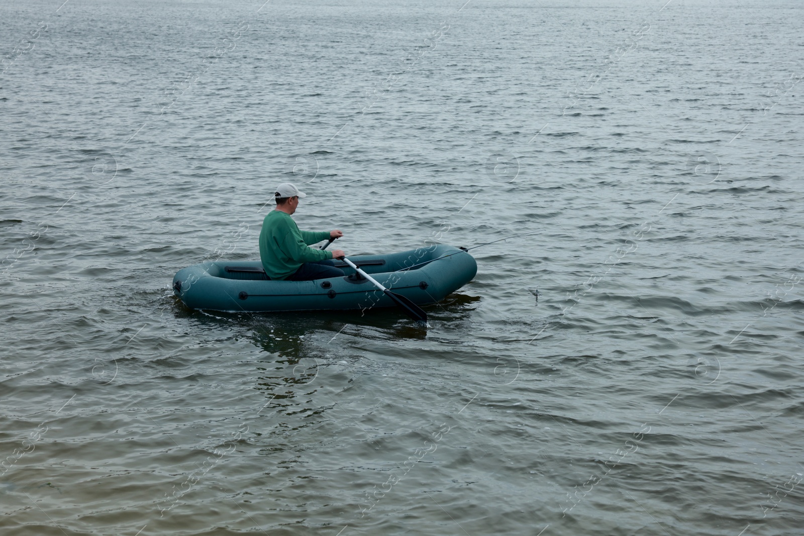 Photo of Man fishing with rod from inflatable rubber boat on river