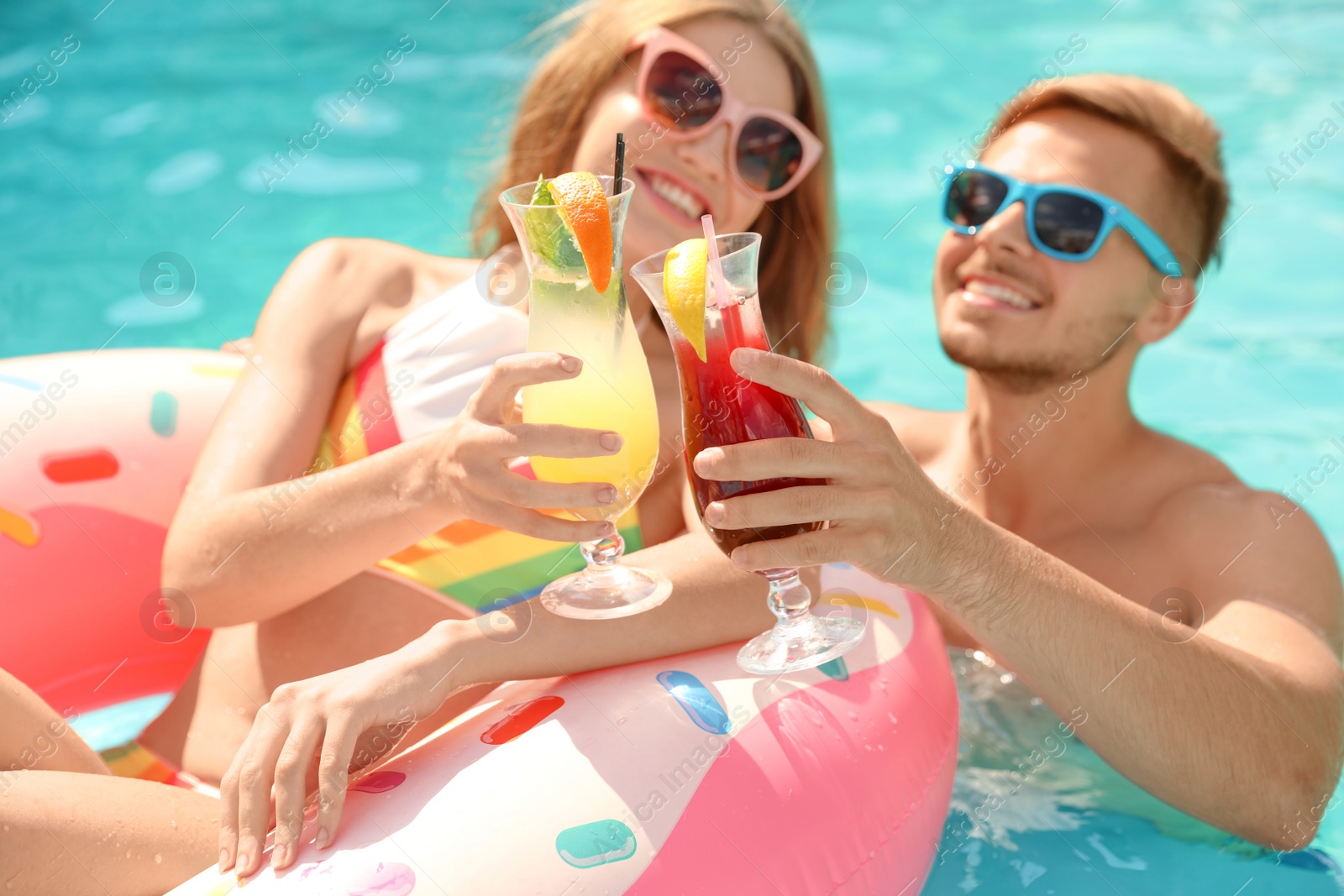 Photo of Young couple with cocktails in pool on sunny day