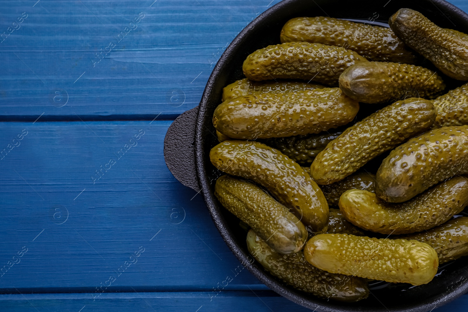 Photo of Serving pan with pickled cucumbers on blue wooden table, top view. Space for text