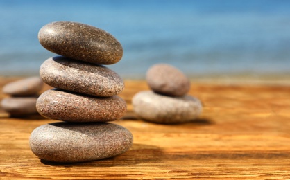 Photo of Stack of stones on wooden table against seascape, space for text. Zen concept