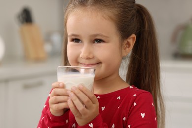 Photo of Cute girl with glass of fresh milk indoors