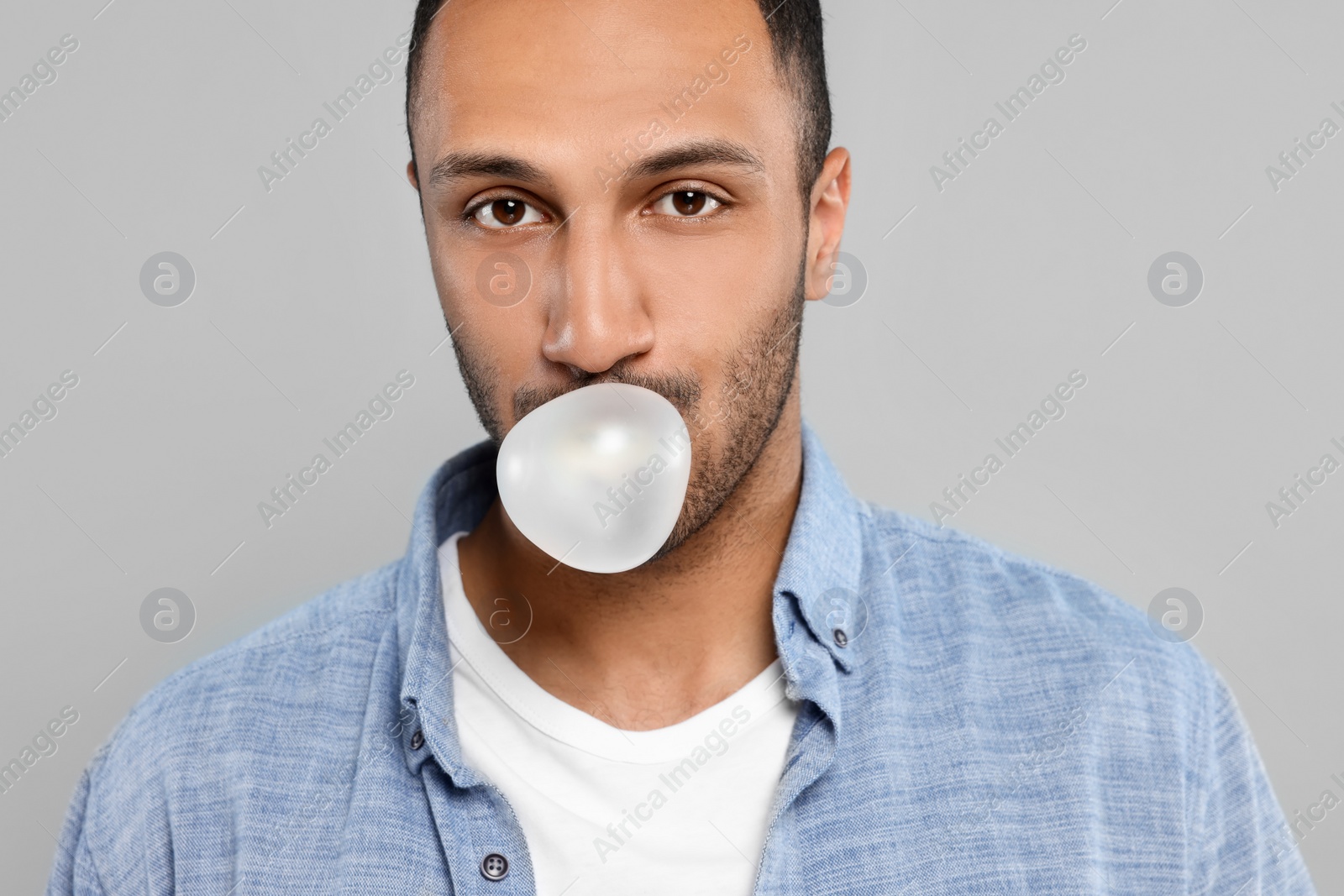 Photo of Portrait of young man blowing bubble gum on light grey background