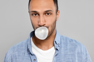 Portrait of young man blowing bubble gum on light grey background