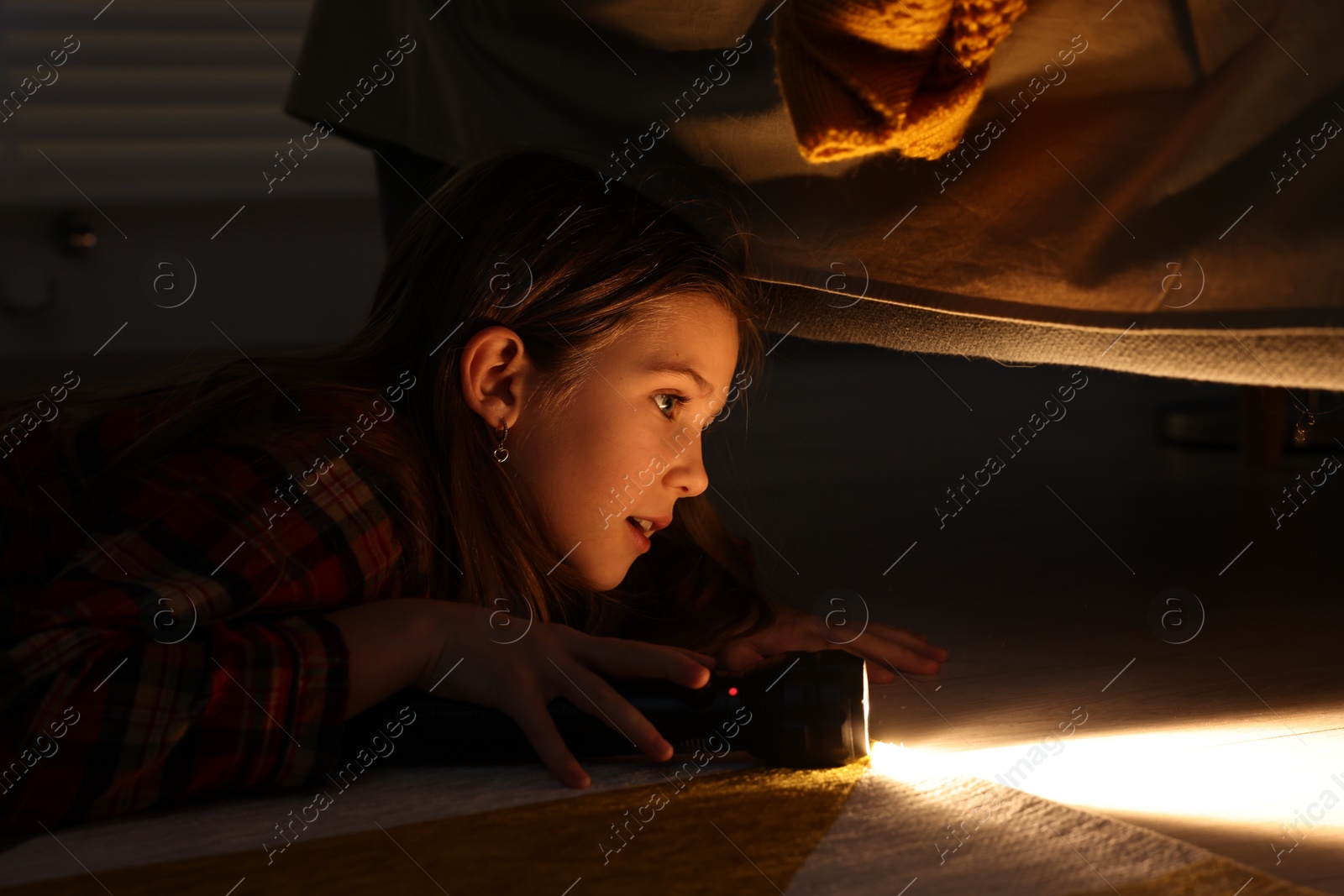 Photo of Little girl with flashlight looking for monster under bed at night