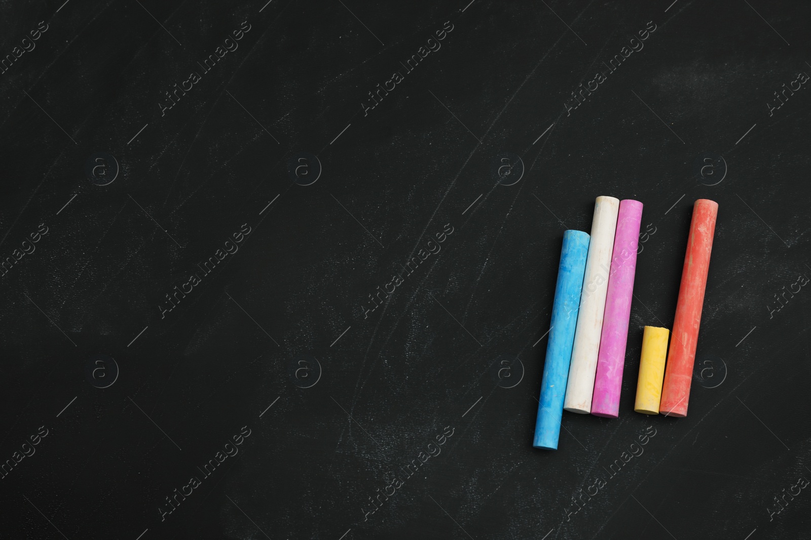 Photo of Colorful chalks on black board, flat lay. Space for text