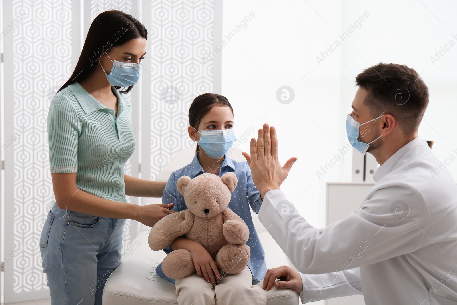 Photo of Mother with daughter visiting pediatrician in hospital. Wearing protective masks