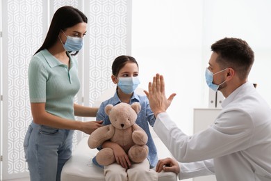 Mother with daughter visiting pediatrician in hospital. Wearing protective masks