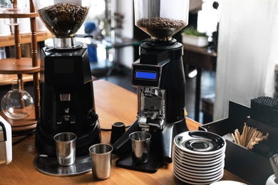 Photo of Modern coffee grinding machines with metal cups and saucers on wooden bar counter