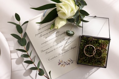 Beautiful wedding rings, boutonniere and invitation on white background, top view