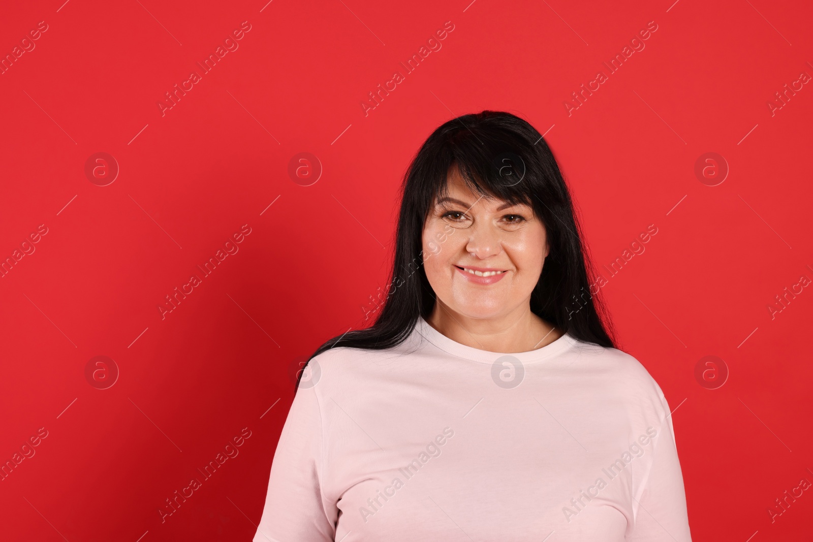 Photo of Beautiful overweight mature woman with charming smile on red background. Space for text