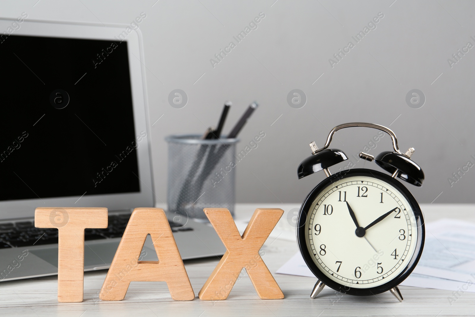 Photo of Word Tax made of wooden letters and alarm clock on white table