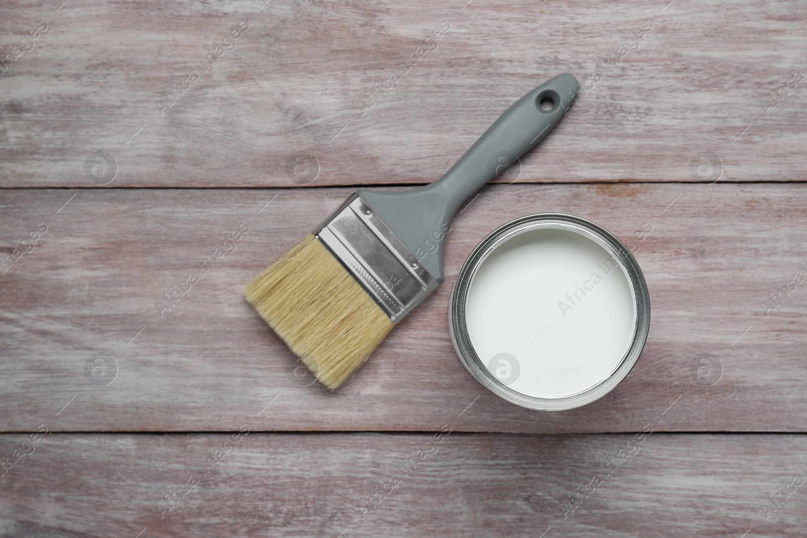 Photo of Can of white paint and brush on wooden table, flat lay