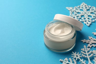 Jar of hand cream and snowflakes on light blue background, space for text. Winter skin care