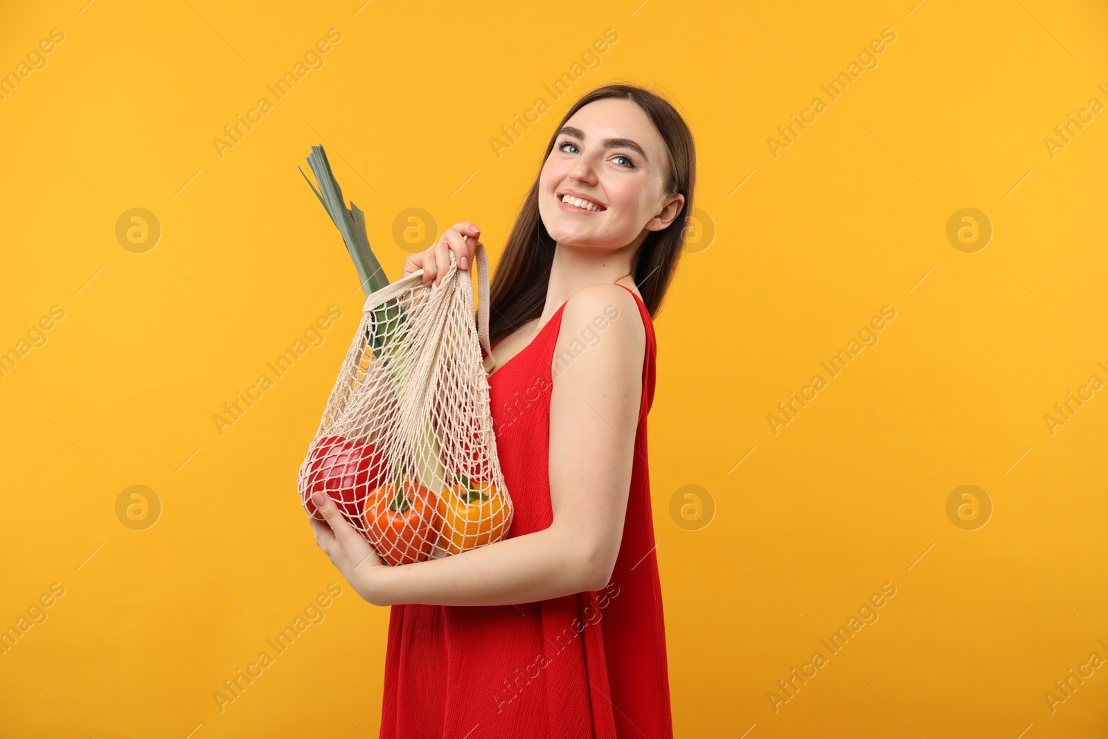 Photo of Woman with string bag of fresh vegetables on orange background