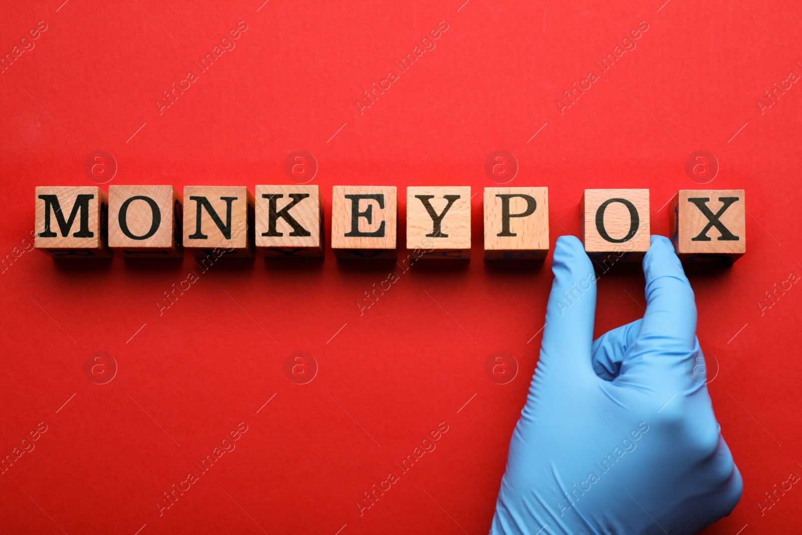 Photo of Nurse making word Monkeypox of wooden cubes on red background, top view