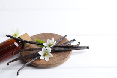 Photo of Vanilla pods, flowers and bottle with essential oil on white wooden table, closeup. Space for text