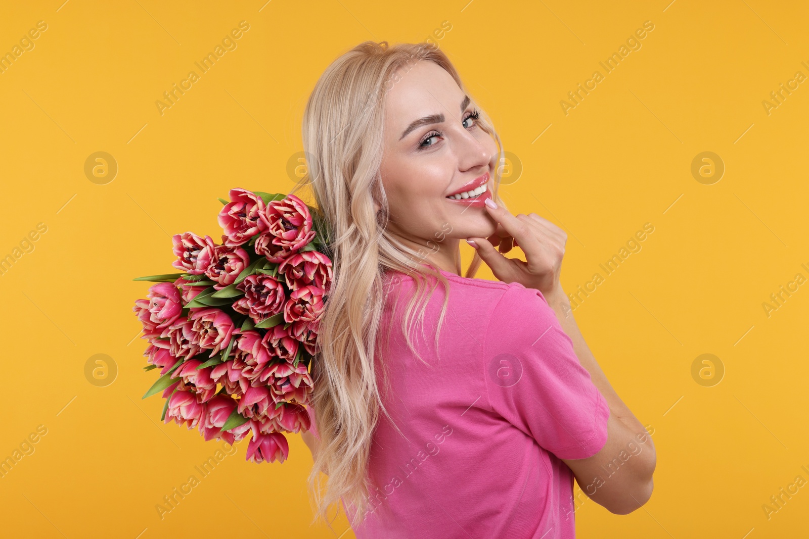 Photo of Happy young woman with beautiful bouquet on orange background