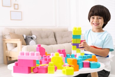 Photo of Cute little boy playing with colorful building blocks at table in living room