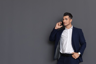 Handsome young man talking on phone against grey background. Space for text