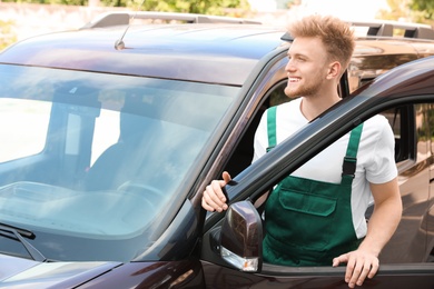 Photo of Young courier in uniform near delivery car outdoors