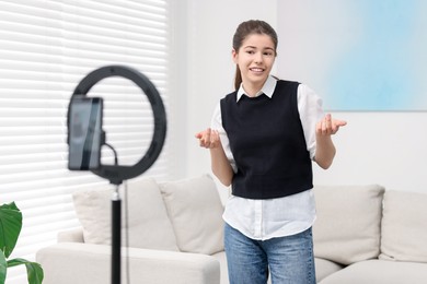 Photo of Smiling teenage blogger explaining something while streaming at home