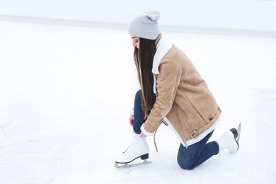 Woman lacing figure skate on ice rink. Space for text