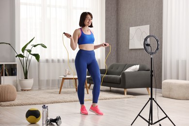 Photo of Happy sports blogger holding skipping rope while streaming online fitness lesson with smartphone at home