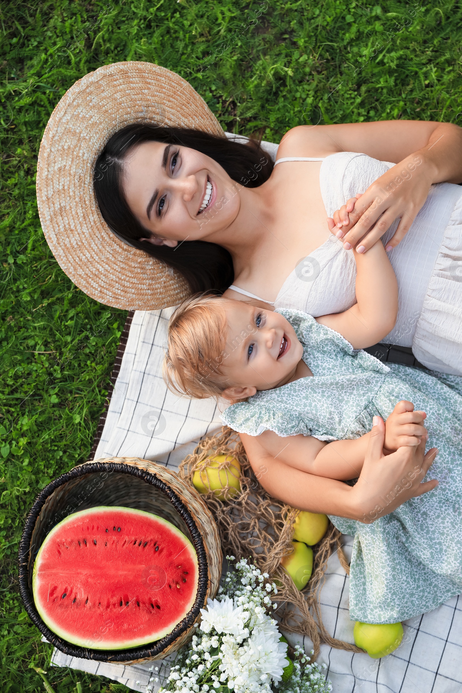 Photo of Mother and her baby daughter resting while having picnic on green grass outdoors, top view