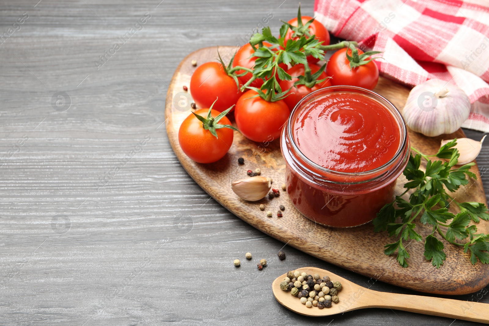 Photo of Tasty ketchup, fresh tomatoes, parsley and spices on grey wooden table, space for text