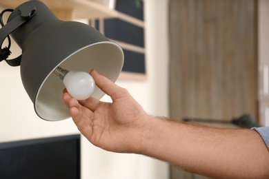 Man changing light bulb in desk lamp indoors, closeup