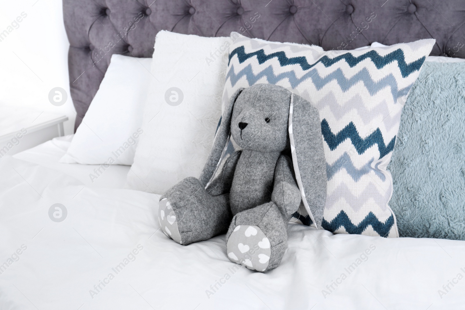 Photo of Cute toy rabbit sitting on bed indoors. Space for text