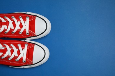 Pair of new stylish red sneakers on blue background, flat lay. Space for text