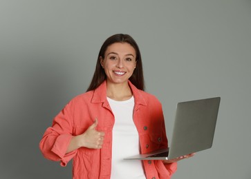 Young woman with modern laptop on grey background